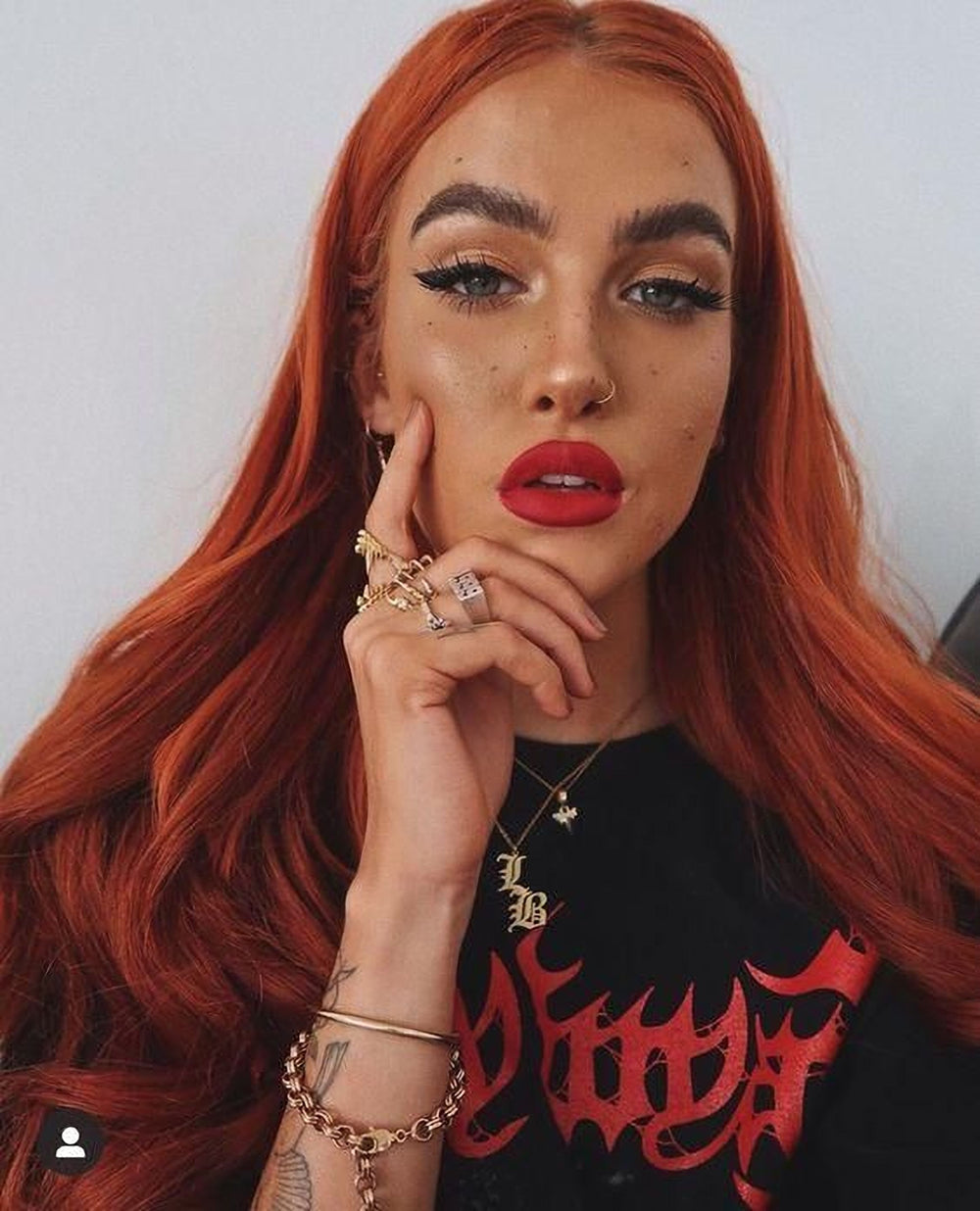 A woman with long, vibrant red hair wearing a black t-shirt with red text, accessorized with multiple rings and bracelets.