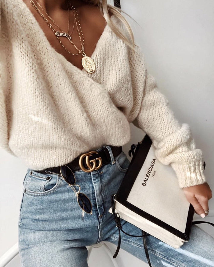 A woman wearing a cream-colored sweater, blue jeans, and a black and white Gucci bag is holding the bag in her hand.
