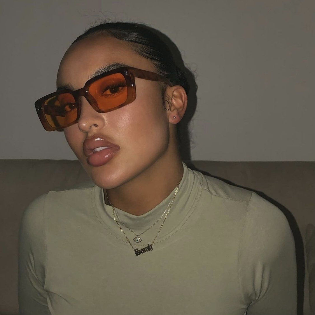 A woman wearing large sunglasses and a necklace is sitting on a couch.