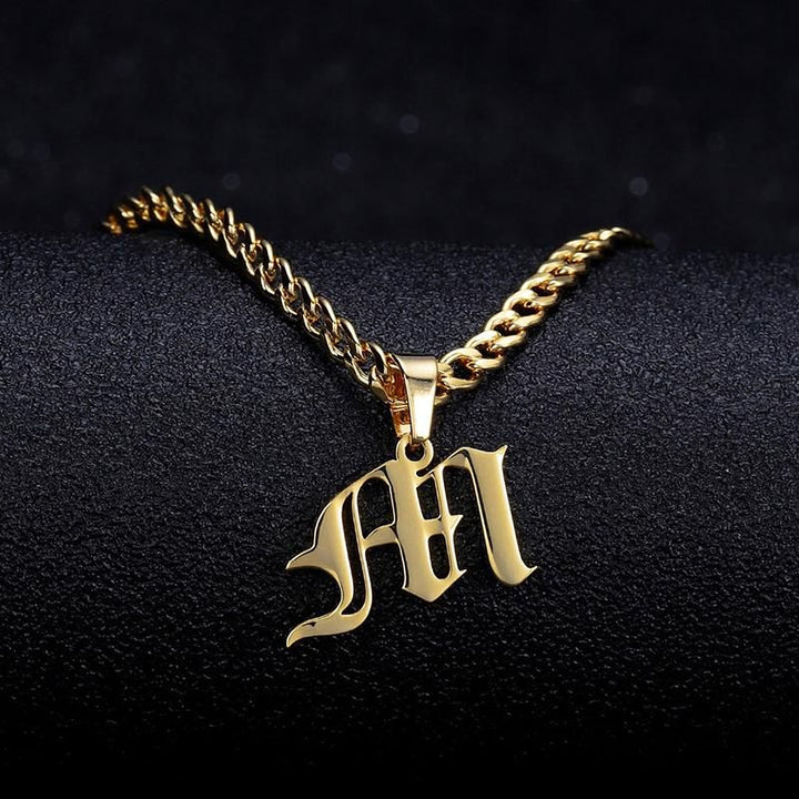 A gold-colored necklace with a pendant featuring the letter "M" in an old-fashioned font.