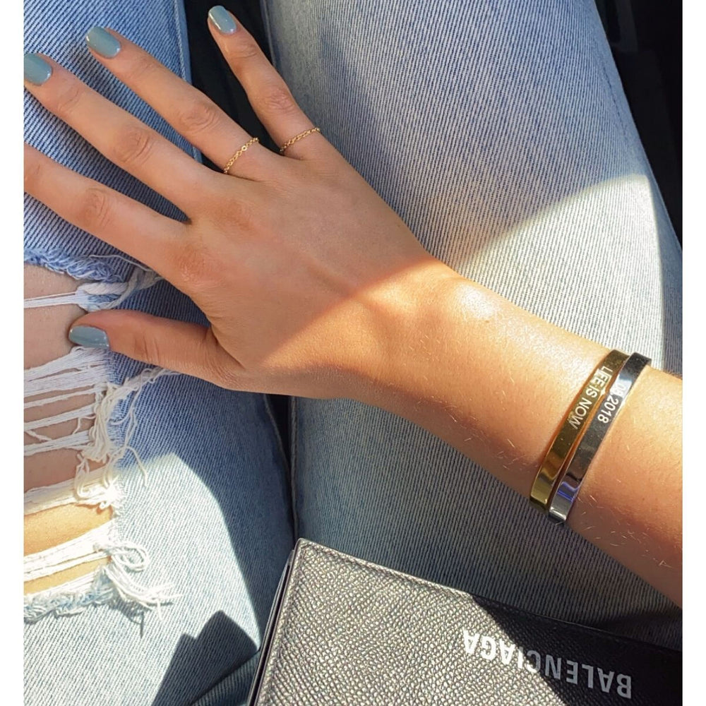 A close-up of a person's hand wearing multiple bracelets and rings, with a denim-style outfit visible in the background.