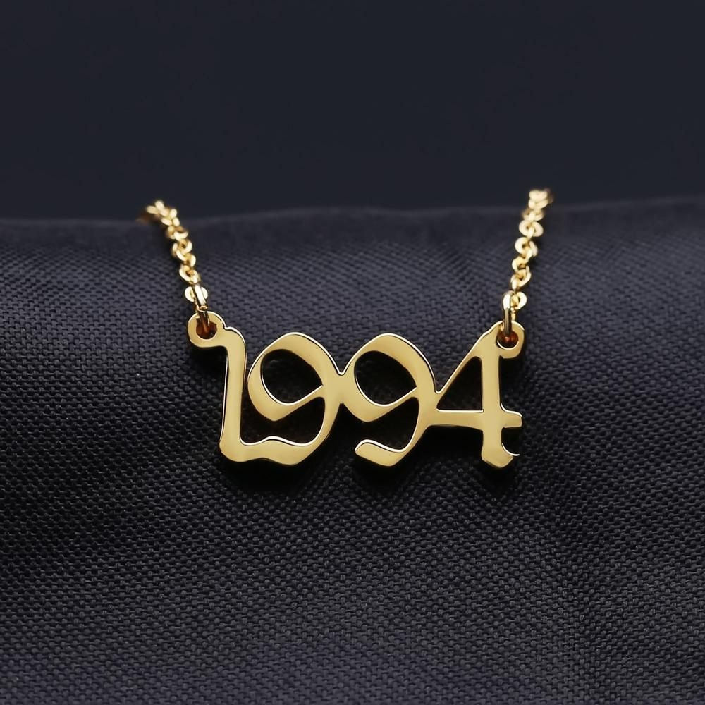 A gold-colored necklace with the year "1994" engraved on it, displayed against a dark background.