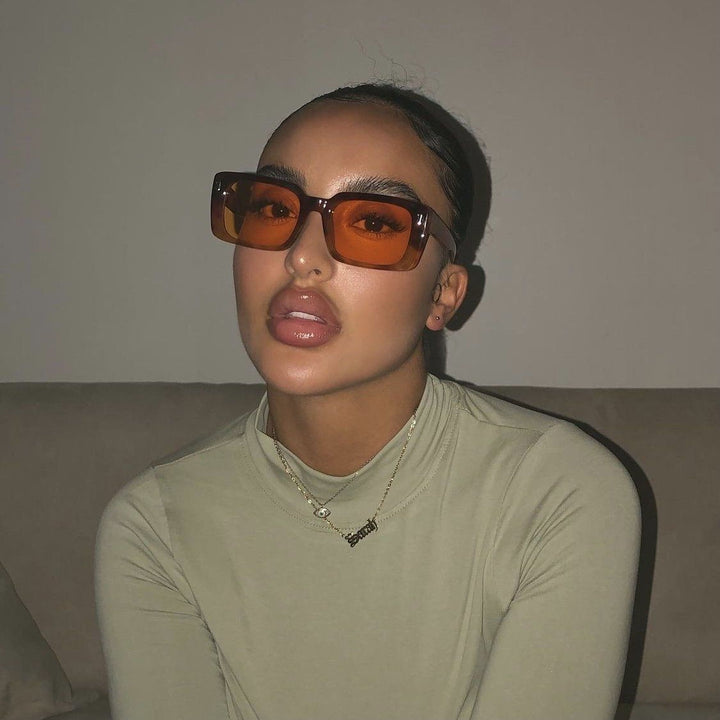 A woman wearing large sunglasses and a necklace is sitting on a couch.