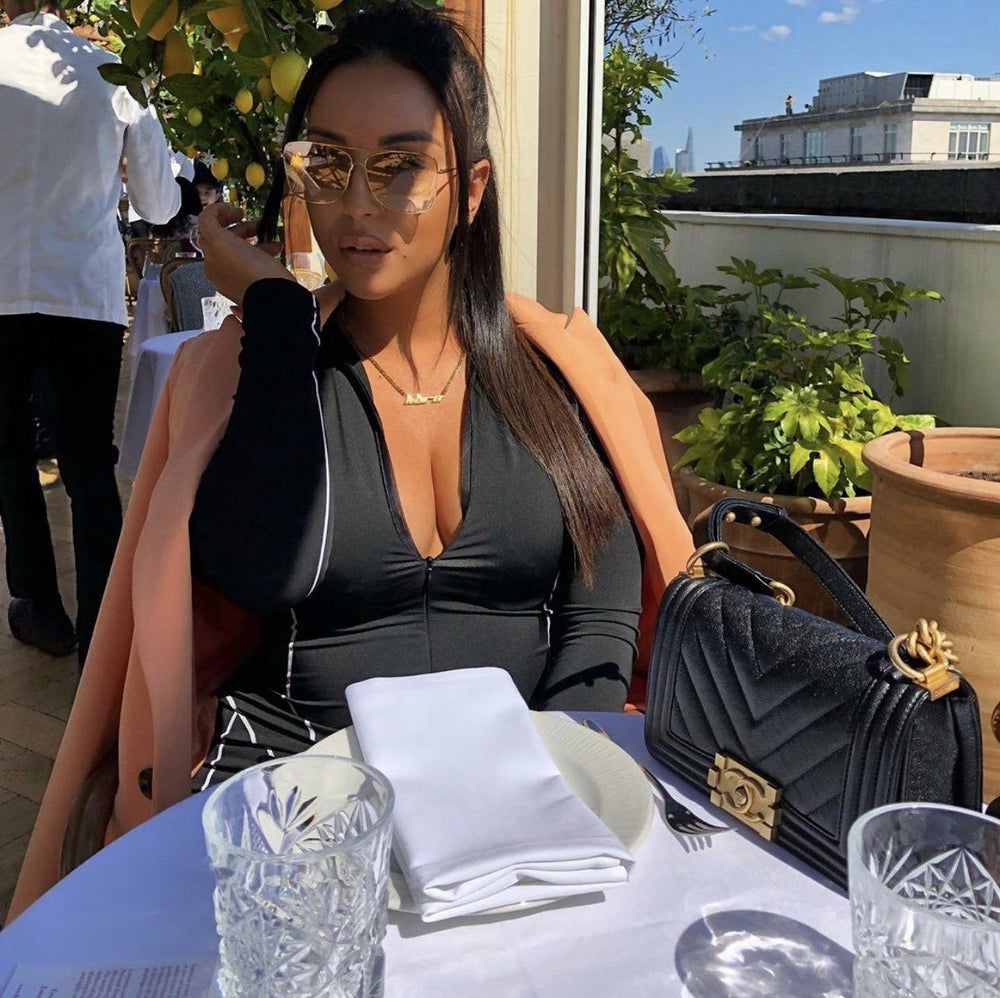 A woman in a black outfit is seated at a table with a glass of water, a white napkin, and a black handbag.