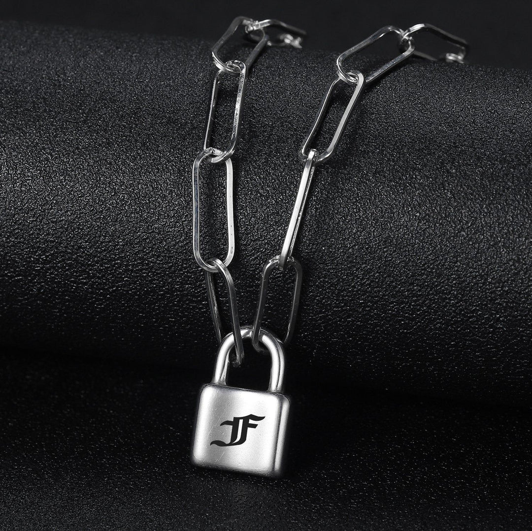 A silver chain necklace with a lock-shaped pendant is displayed against a dark background.