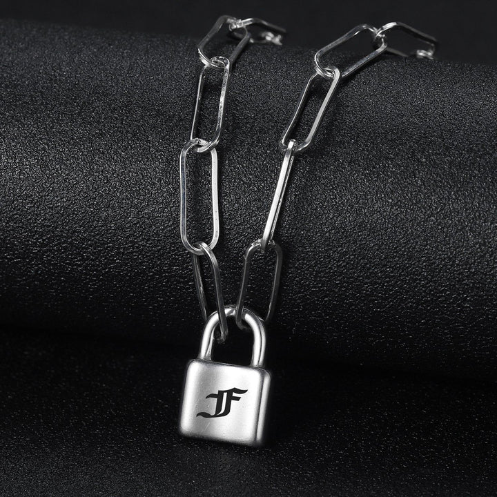A silver chain necklace with a lock-shaped pendant is displayed against a dark background.