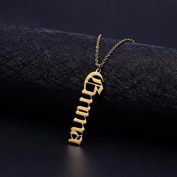 A gold-colored necklace with a pendant in the shape of the word "Gemma" is displayed against a dark background.
