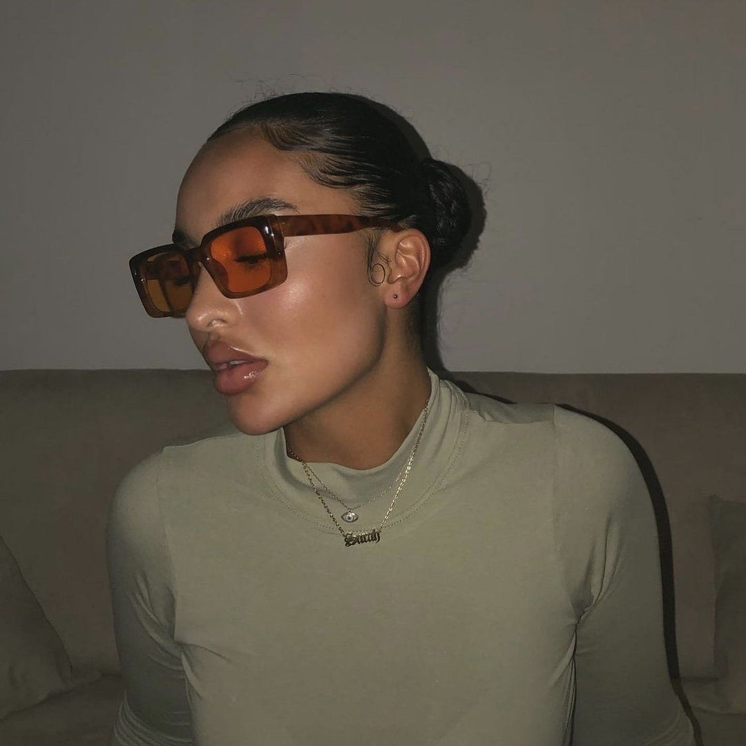 A woman wearing large sunglasses and a necklace is sitting on a couch.