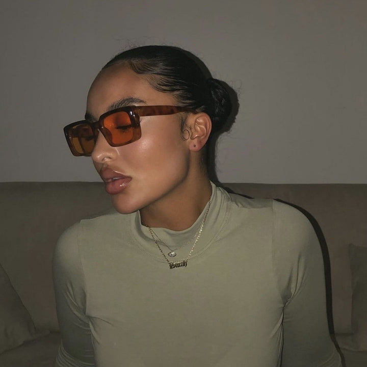 A woman wearing large sunglasses and a necklace is sitting on a couch.