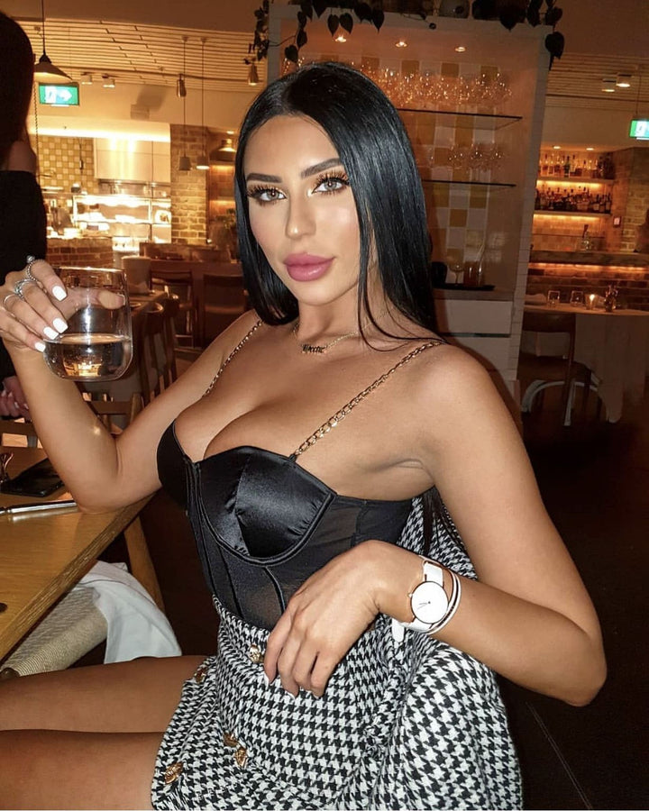 A woman with long dark hair wearing a black and white patterned skirt and holding a glass of wine, posing in a restaurant setting.