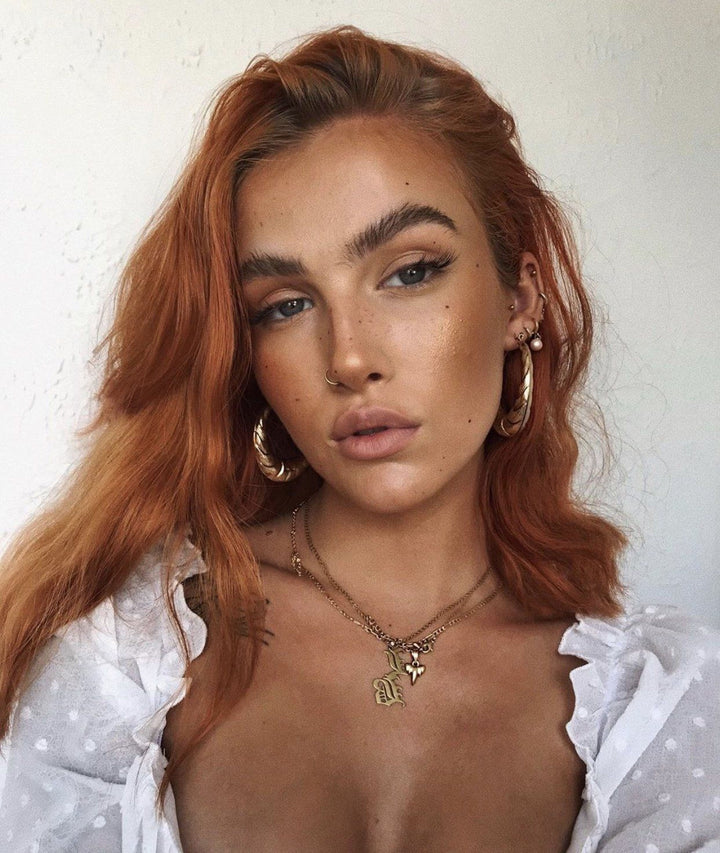 A close-up portrait of a woman with long, reddish-brown hair and a pensive expression, wearing a white blouse and large hoop earrings.