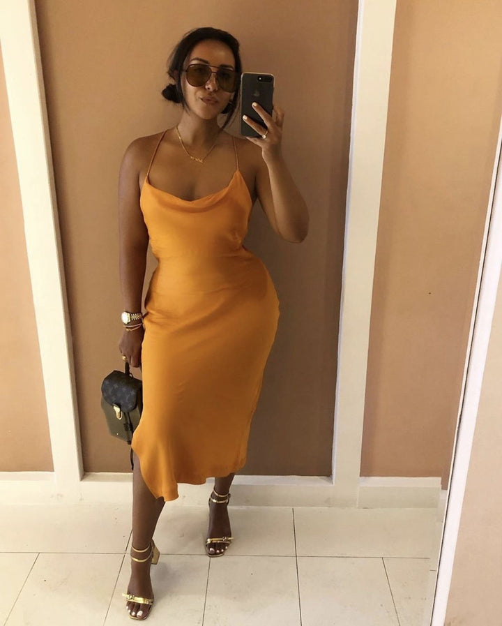 A woman wearing a yellow dress and sunglasses is taking a selfie with a smartphone.
