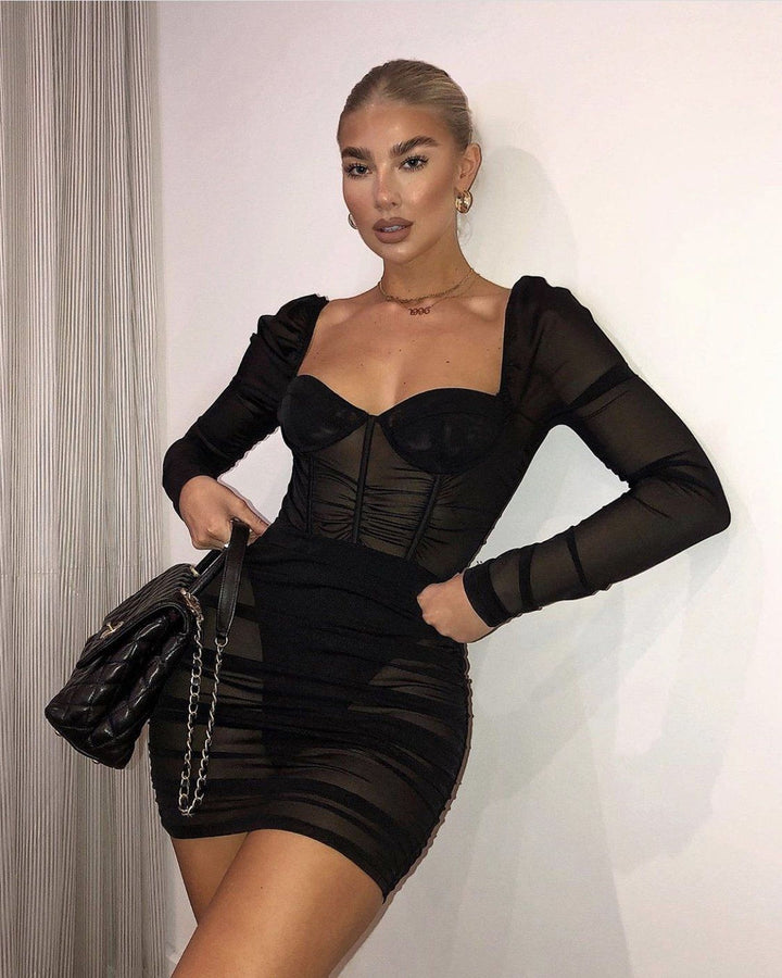 A woman wearing a black dress with puffed sleeves and a fitted bodice, posing confidently with her hands on her hips.