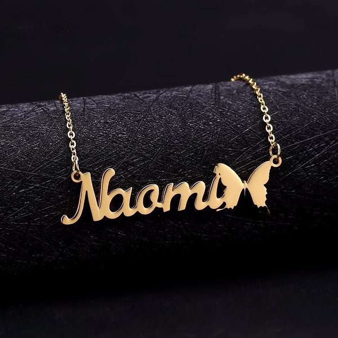 A gold-colored personalized name necklace with the name "Nora" engraved on it, featuring a butterfly design.