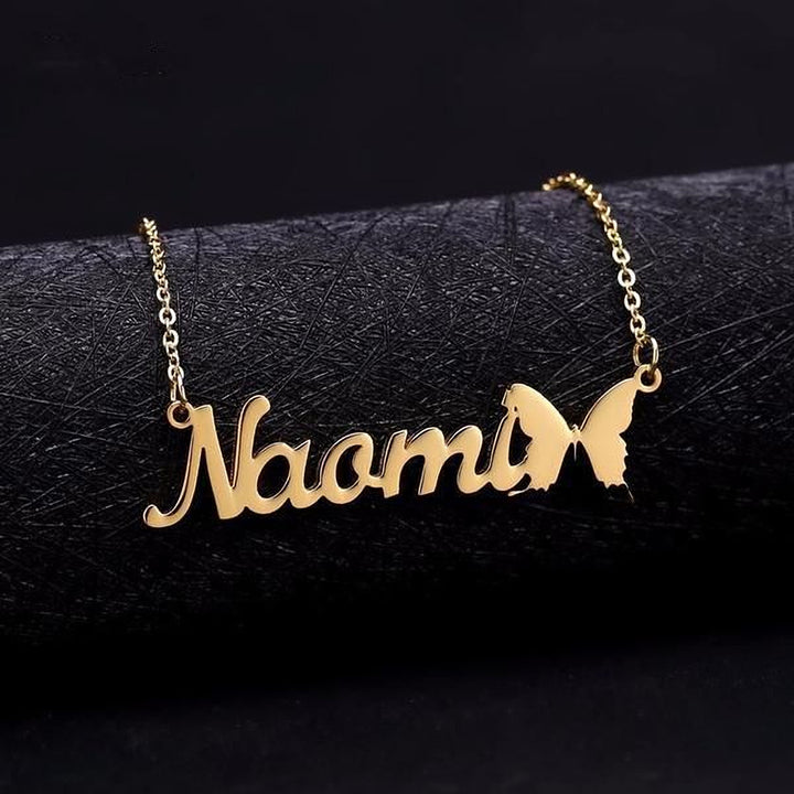 A gold-colored personalized name necklace with the name "Nora" engraved on it, featuring a butterfly design.