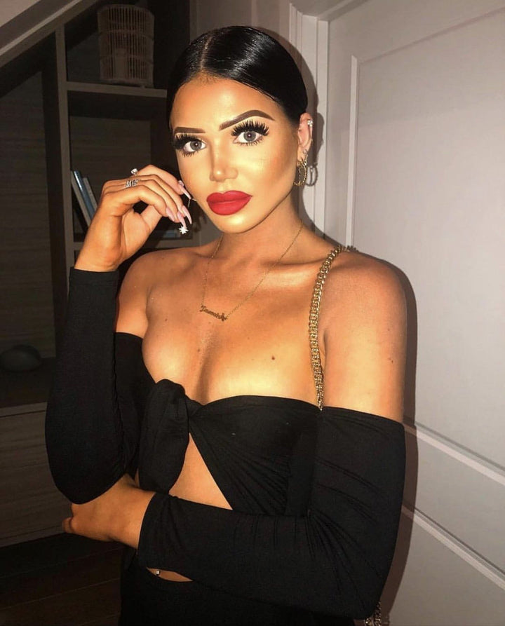 A woman wearing a black off-the-shoulder dress with a gold chain strap, posing for a photograph.