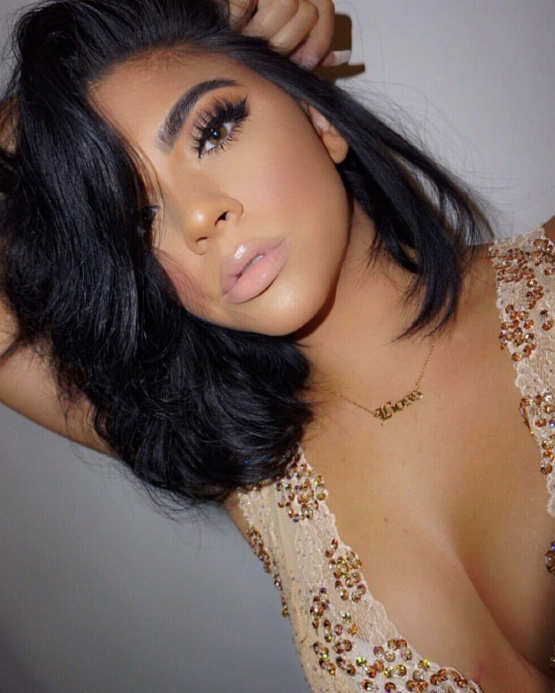 A close-up portrait of a woman with dark hair and makeup, wearing a gold sequined dress.